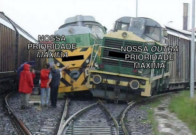 Dois trens colidem lateralmente em uma junção de trilhos. Um deles tem a legenda 'Nossa prioridade máxima', e o outro 'Nossa OUTRA prioridade máxima'