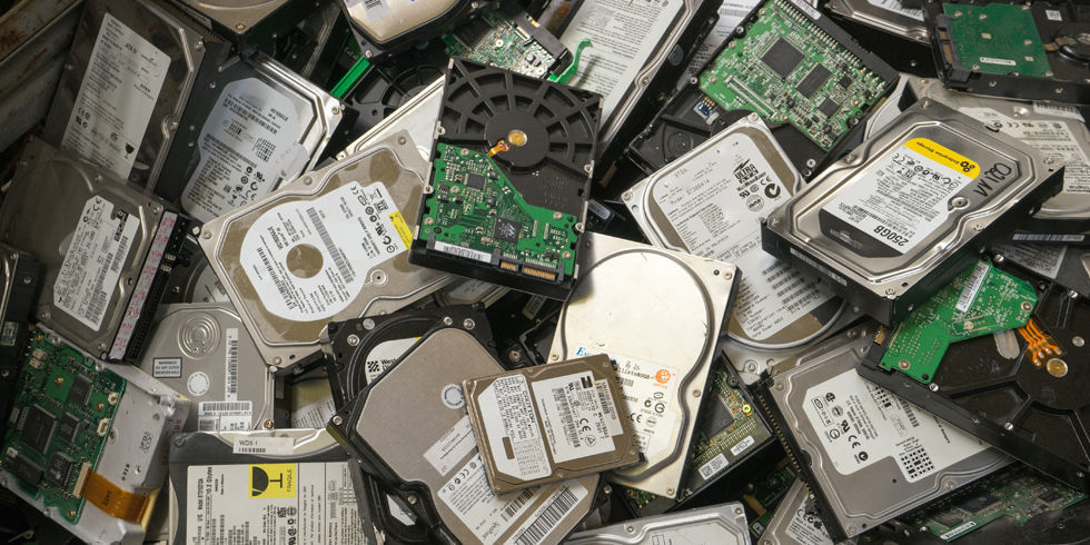 Foto jornalística de dezenas de discos rígidos desordenadamente largados sobre uma superfície.