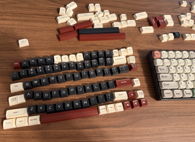 Um jogo de teclas chamado Rome, com teclas em cor preta, e algumas em cor creme e cor vinho, gerando um contraste meio vintage. As teclas estão soltas e espalhadas, em ordem, sobre uma mesa.