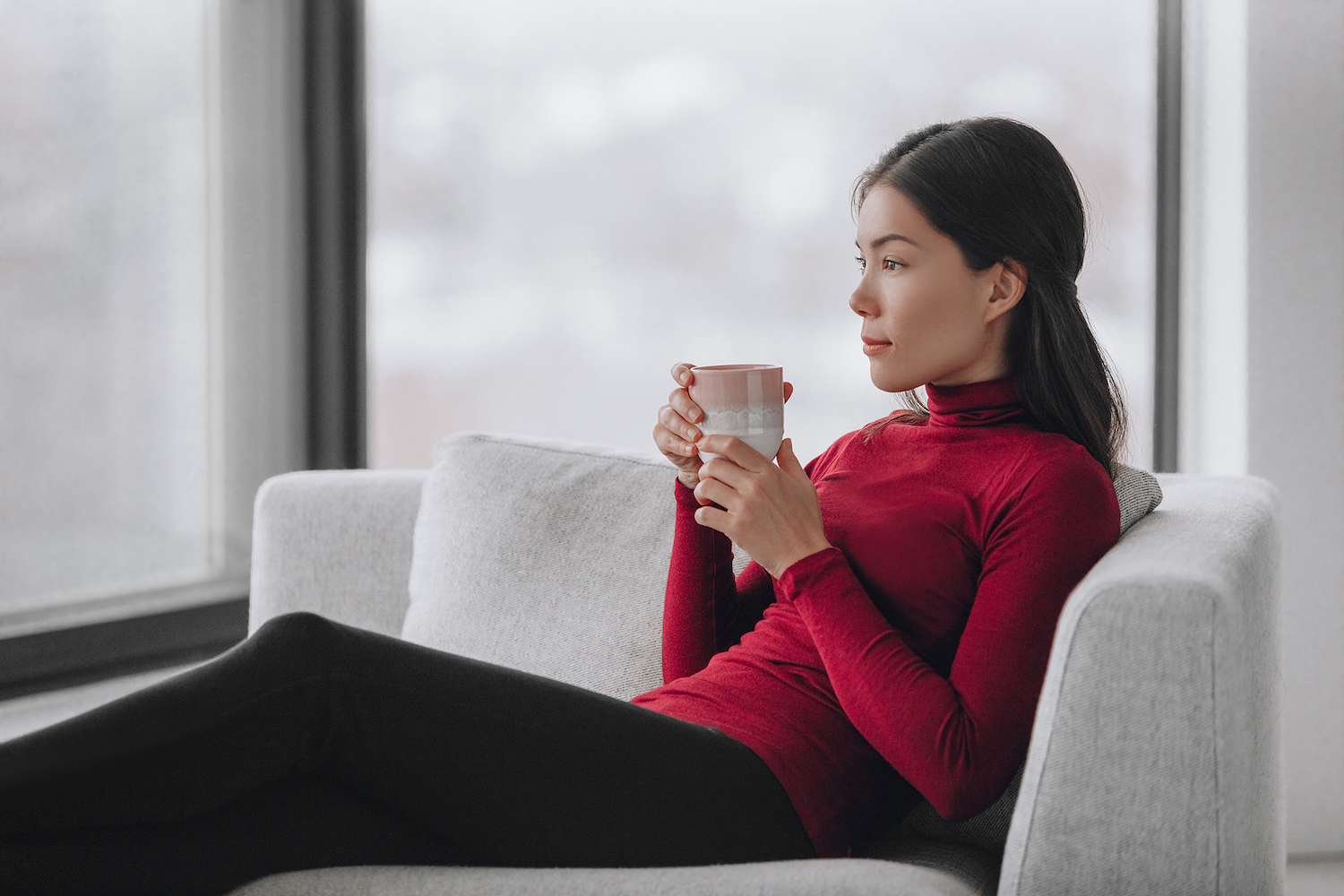 Mulher no sofá, em posição confortável, rosto relaxado, segurando uma xícara