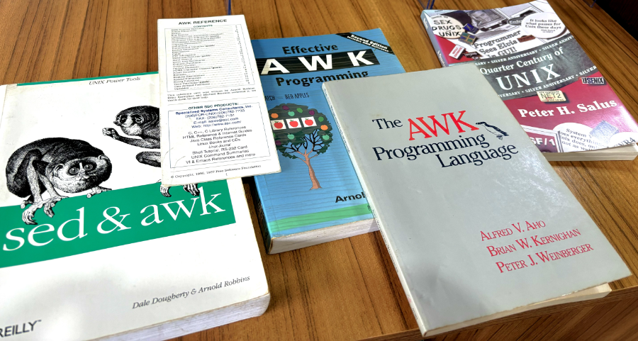 Lado a lado na minha mesa, 3 livros e um cartão de referência da linguagem Awk, e um livro sobre a história do Unix, todos do século passado