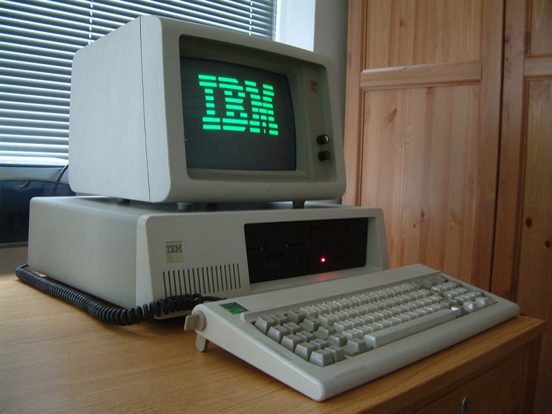 IBM PC XT exibindo a palavra IBM em letras grandes na tela monocromática de fósforo verde, e com o HD de 10MB original, que ocupava duas baias verticais de 5¼.