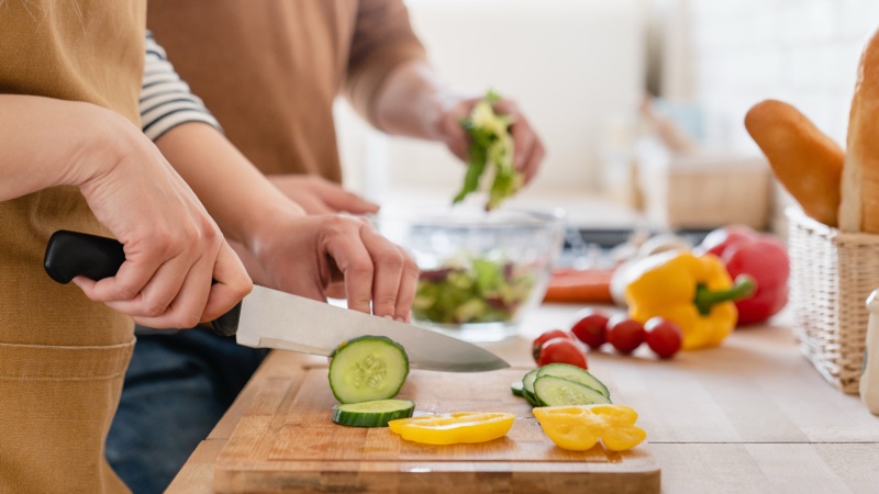 Foto de uma mulher picando legumes sobre uma tábua de corte