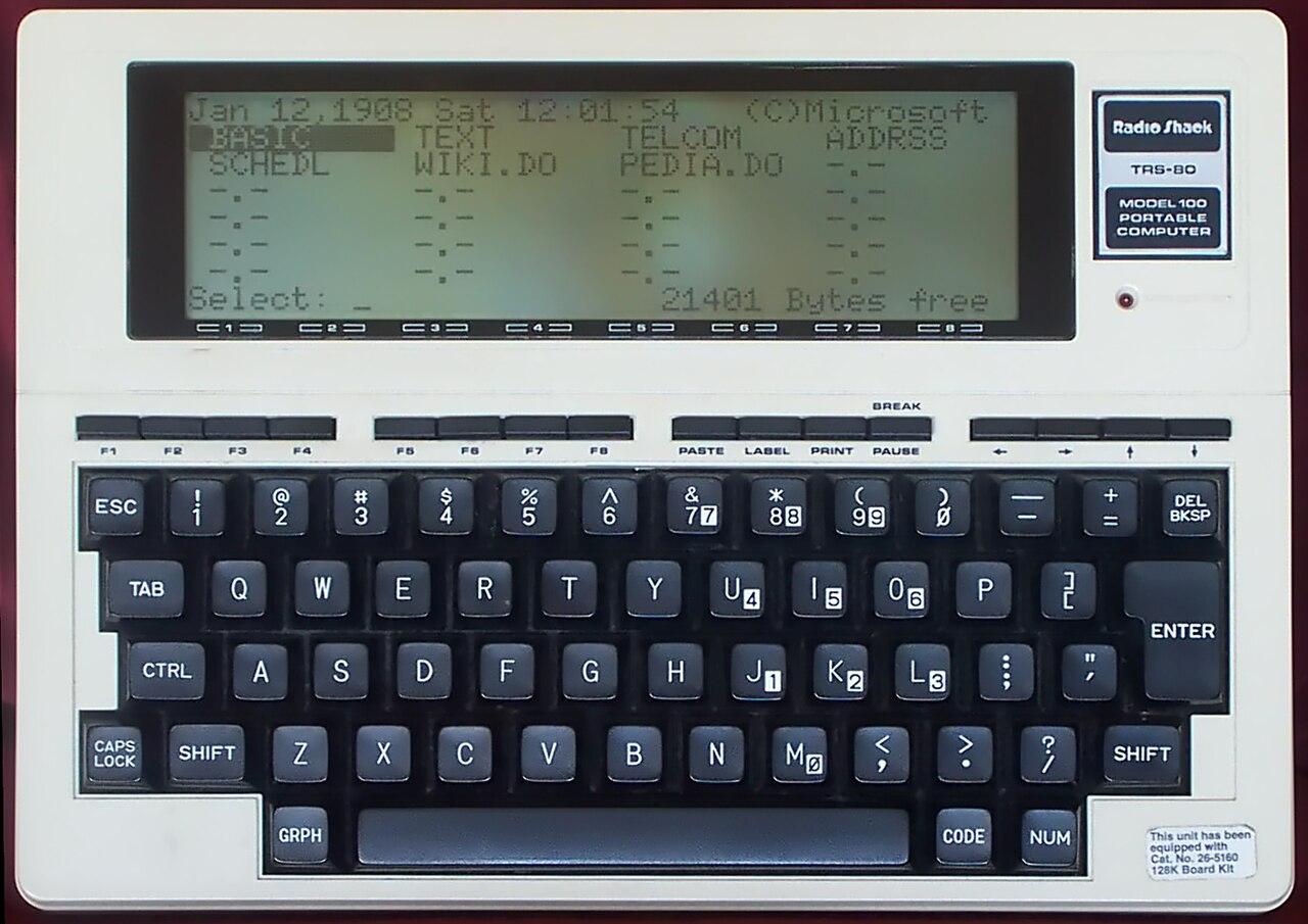 Foto de um TRS-80 modelo 100, com seu teclado típico dos anos 80, e tela LCD de apenas 8 linhas em modo texto.